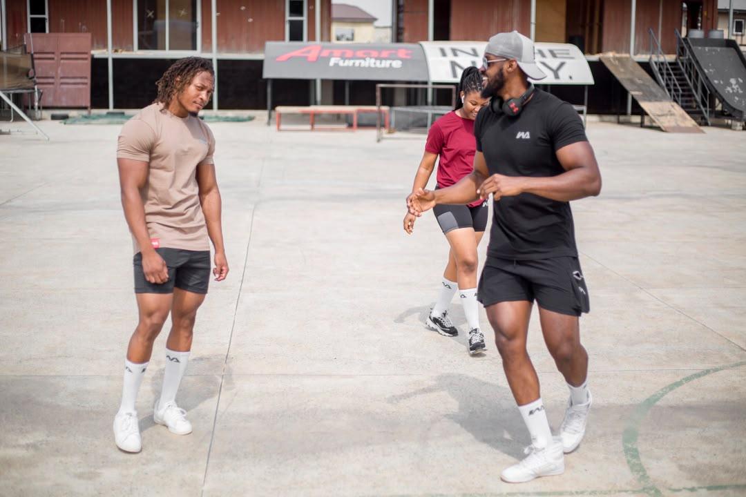 Three people in Warmz tees — tan, maroon, and black — walking across an outdoor concrete court.