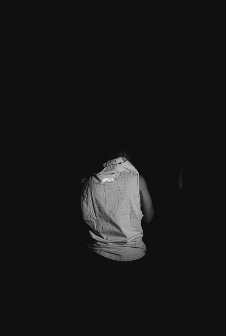 A woman seen from behind in a grey Warmz sleeveless hoodie with the WA logo across the shoulder blades, in dramatic black-and-white lighting.